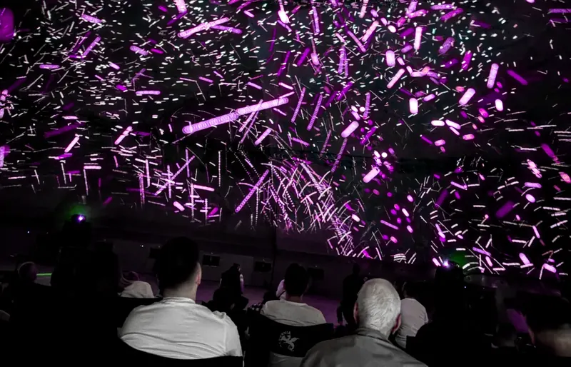 Zuschauer im Kino 360 unter einer violett-rosafarbenen Projektion auf der Kuppel